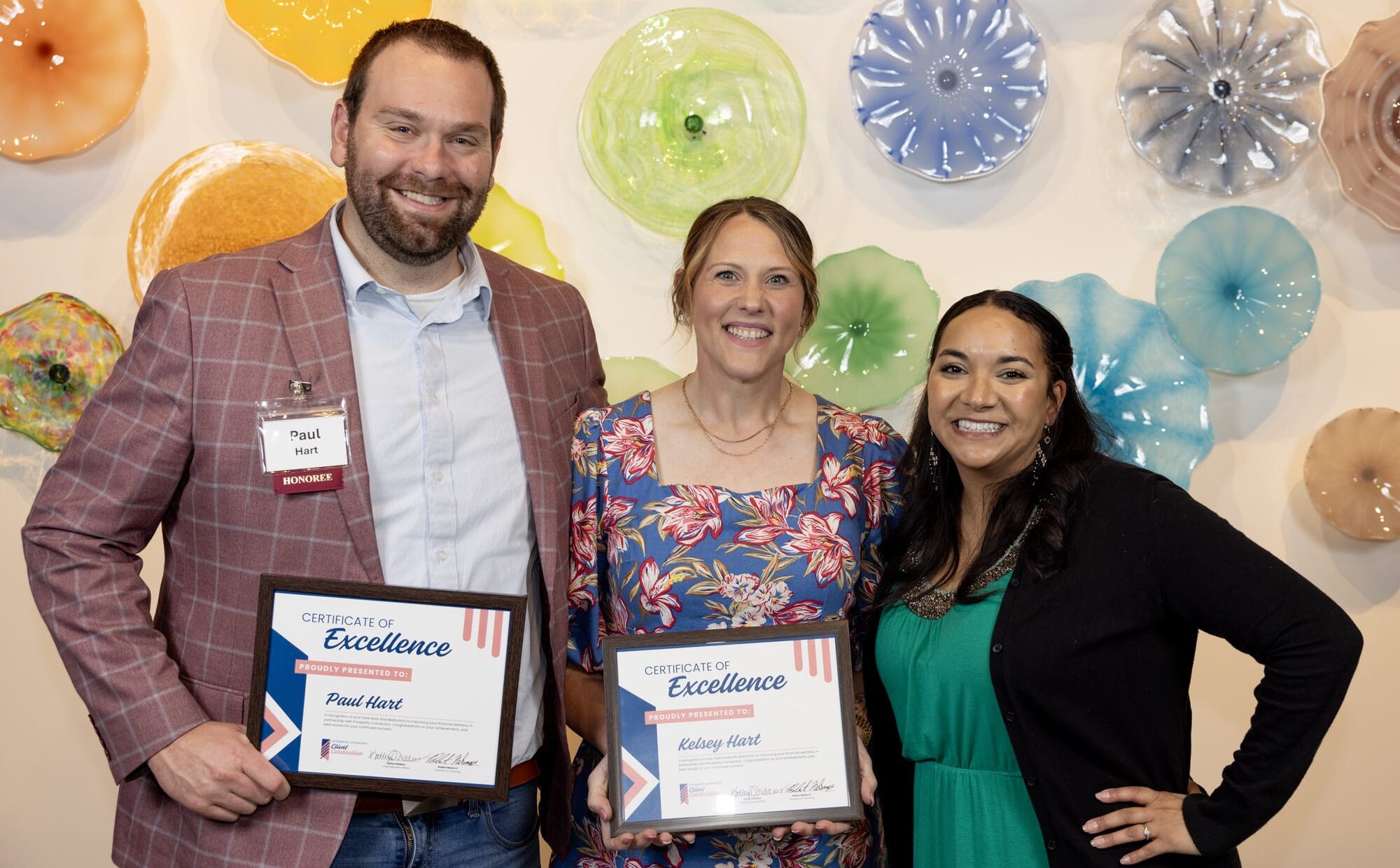 Paul and Kelsey Hart holding up their Certificate of Excellence while standing next to their financial coach, Ashlee Morgan.