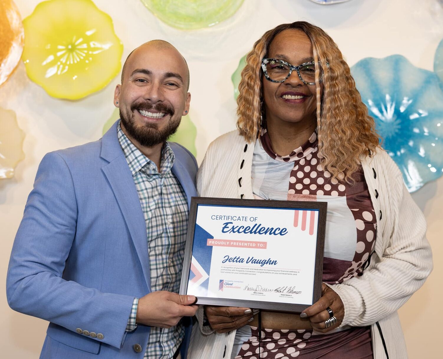 Jetta smiles while holding her Certificate of Excellence. She poses for a picture with her financial coach, Pablo.