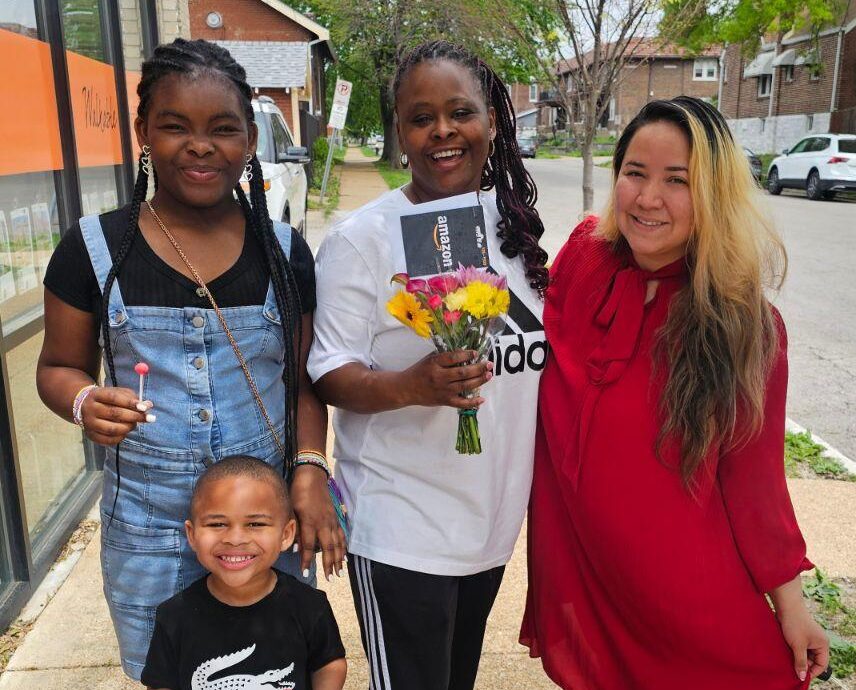 DeAiris smiles and holds flowers that Veronica brought her. They are standing with her kids after closing on her house!